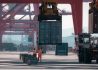 Two workers in orange safety vests loading containers onto a cargo ship.