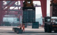 Two workers in orange safety vests loading containers onto a cargo ship.